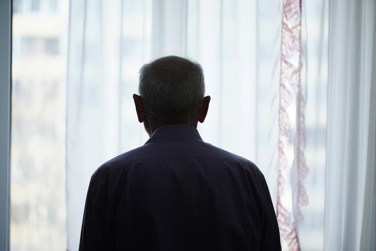 Un homme d'âge mûr, pensif, regardant par une fenêtre, illustrant la solitude en famille.