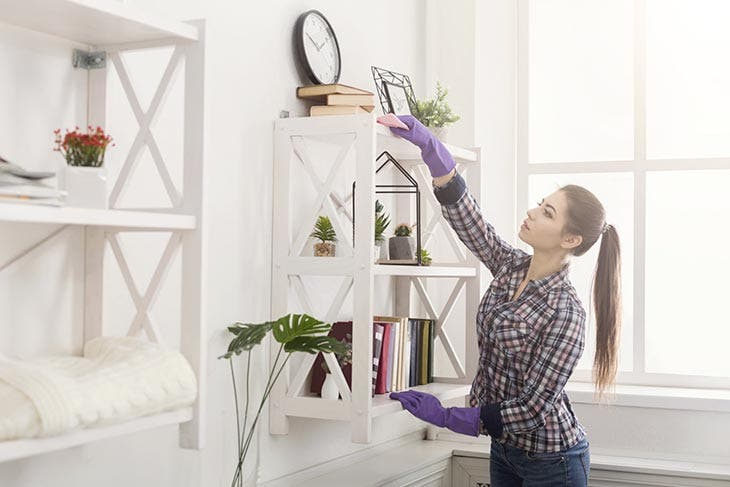 Femme dépoussiérant une étagère 