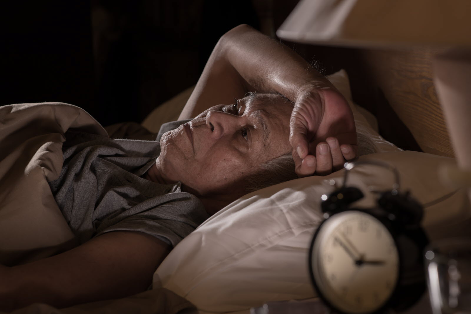 Une personne âgée regardant par la fenêtre à l'aube, illustrant un réveil précoce.