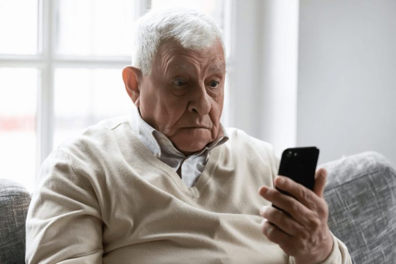 Un homme âgé semble perplexe, tenant un téléphone portable. Cette image illustre la confusion que peut générer la complexité des démarches administratives.