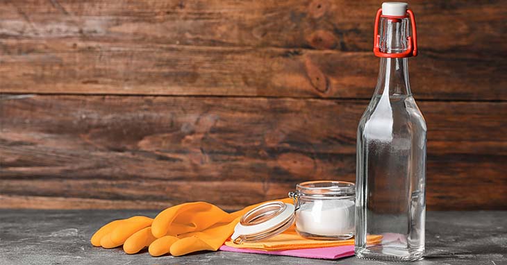 Produits de nettoyage maison : une bouteille de vinaigre blanc et un flacon d'assouplissant posés sur un sol propre.